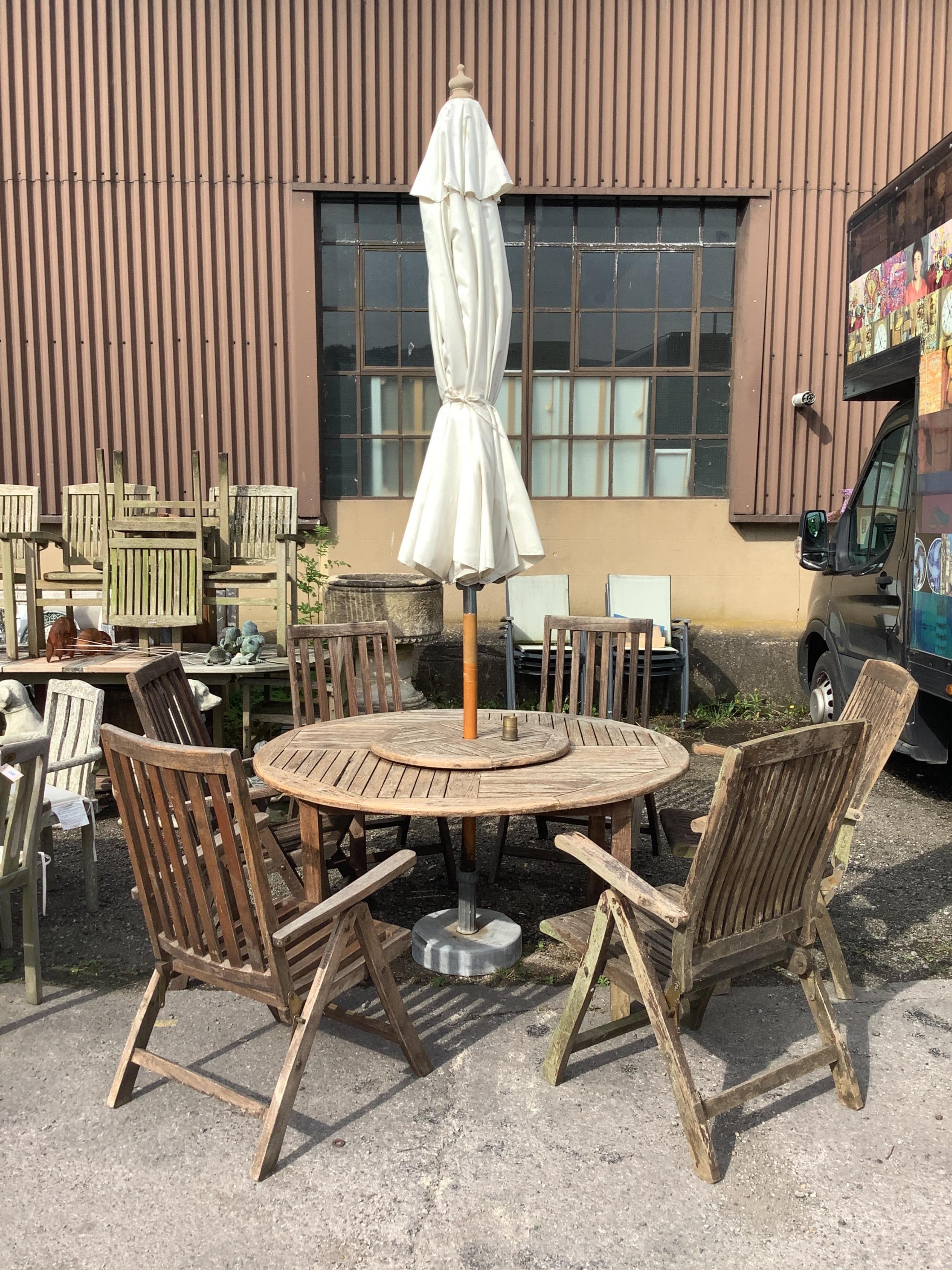 A circular weathered teak garden table with lazy Susan, diameter 150cm, height 75cm, a crank parasol and six (four plus two) folding armchairs. Condition - fair